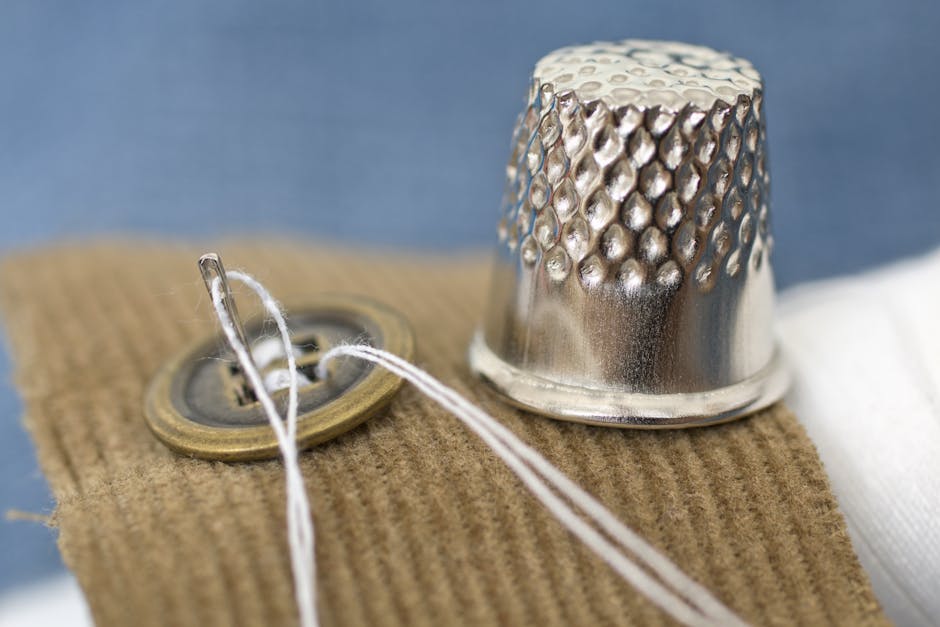 A detailed macro shot of a sewing button and thimble on fabric, illustrating tailoring tools.