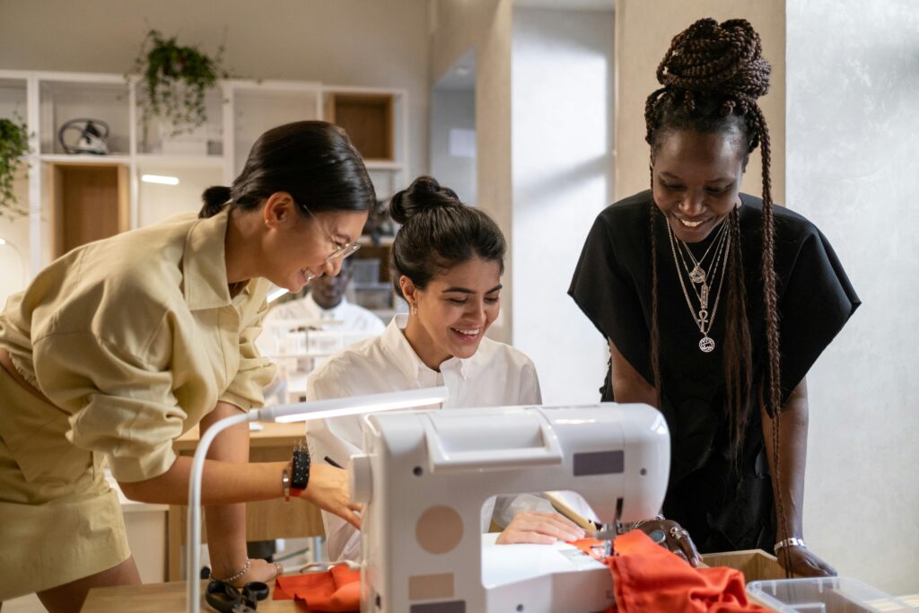 Three women collaborate joyfully in a sewing workshop, focusing on creating fashion pieces.